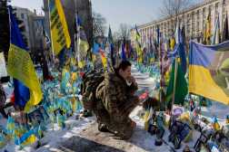 A serviceman kneels down next  at a makeshift memorial for the Ukrainian and foreign fighters at Independence Square in Kyiv, on February 24, 2025, during the third anniversary of Russia's invasion of Ukraine. (Photo by Tetiana DZHAFAROVA / AFP)