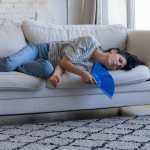 Enferma frustrada mujer adulta dueña de casa que recibe golpes de calor, tendida en el sofá, agitando un ventilador de papel de mano, sufriendo de aire sofocante, agotamiento, hipoxia, sobrecalentamiento, mal, mal