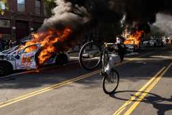 A demonstrator rides a bicycle past burning Waymo vehicles as protesters clash with law enforcement near the federal building during a protest in response to federal immigration operations in Los Angeles, California, on June 8, 2025. US President Donald Trump deployed 2,000 troops on June 7 to handle escalating protests against immigration enforcement raids in the Los Angeles area, a move the state's governor termed "purposefully inflammatory." Federal agents clashed with angry crowds in a Los Angeles suburb as protests stretched into a second night Saturday, shooting flash-bang grenades and shutting part of a freeway amid raids on undocumented migrants, reports said. (Photo by ETIENNE LAURENT / AFP)