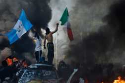 LOS ANGELES, CALIFORNIA - JUNE 08: Protestors wave flags as burning and vandalized Waymo cars line the street on June 08, 2025 in Los Angeles, California. Tensions in the city remain high after the Trump administration called in the National Guard against the wishes of city leaders following two days of clashes with police during a series of immigration raids.   Mario Tama/Getty Images/AFP (Photo by MARIO TAMA / GETTY IMAGES NORTH AMERICA / Getty Images via AFP)