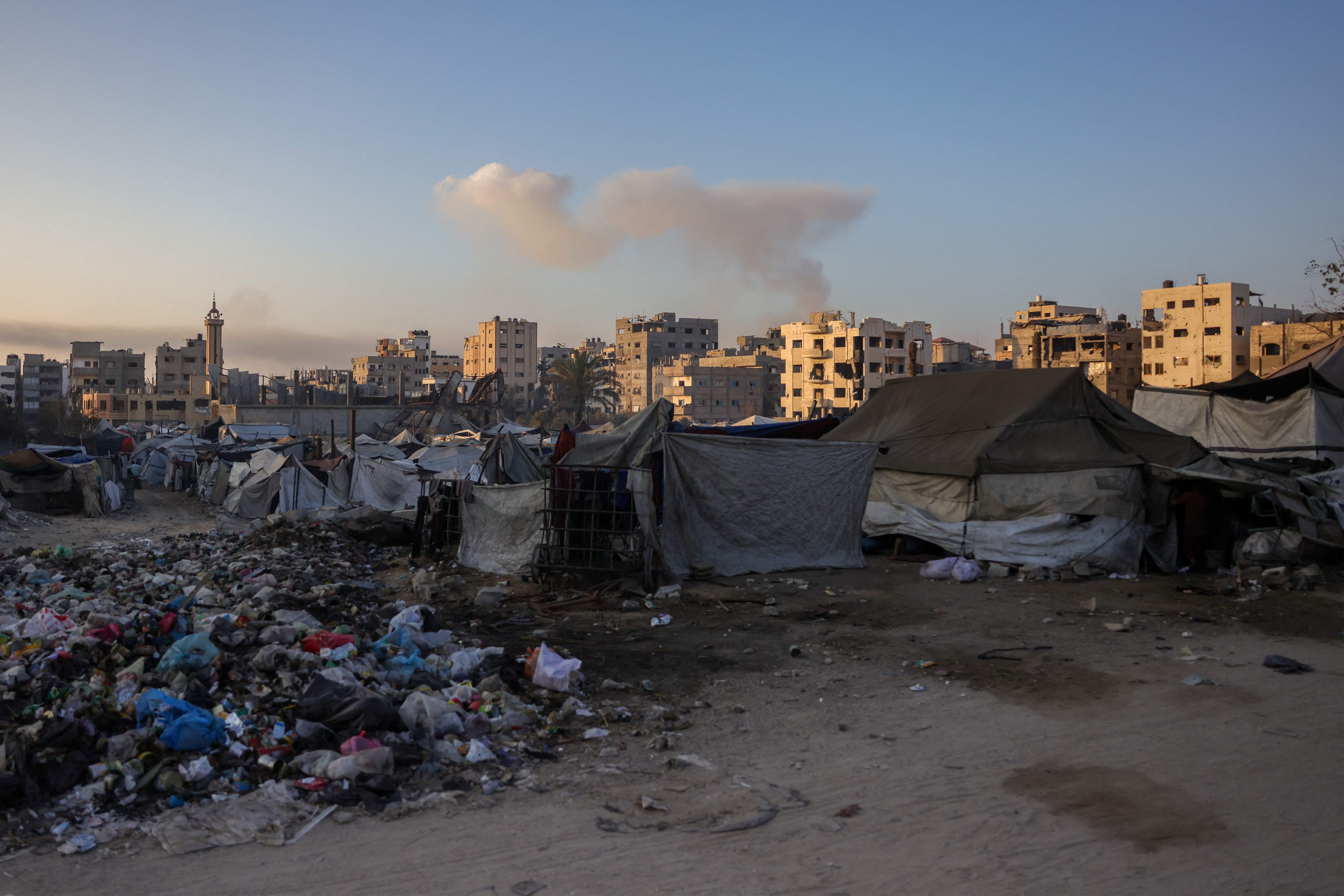 This picture shows shelters and rubbish in Jabalia, in the northern Gaza Strip, as smoke billows on the horizon during Israeli bombardment on August 25, 2025. Israeli Defence Minister Israel Katz vowed on August 22, to destroy Gaza City if Hamas did not agree to disarm, release all remaining hostages in the territory and end the war on Israel's terms. (Photo by BASHAR TALEB / AFP)