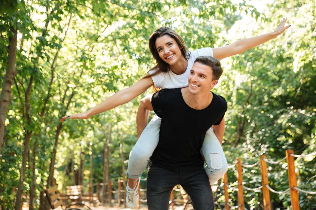 Young smiling couple enjoying piggyback ride and laughing at the park outdoors