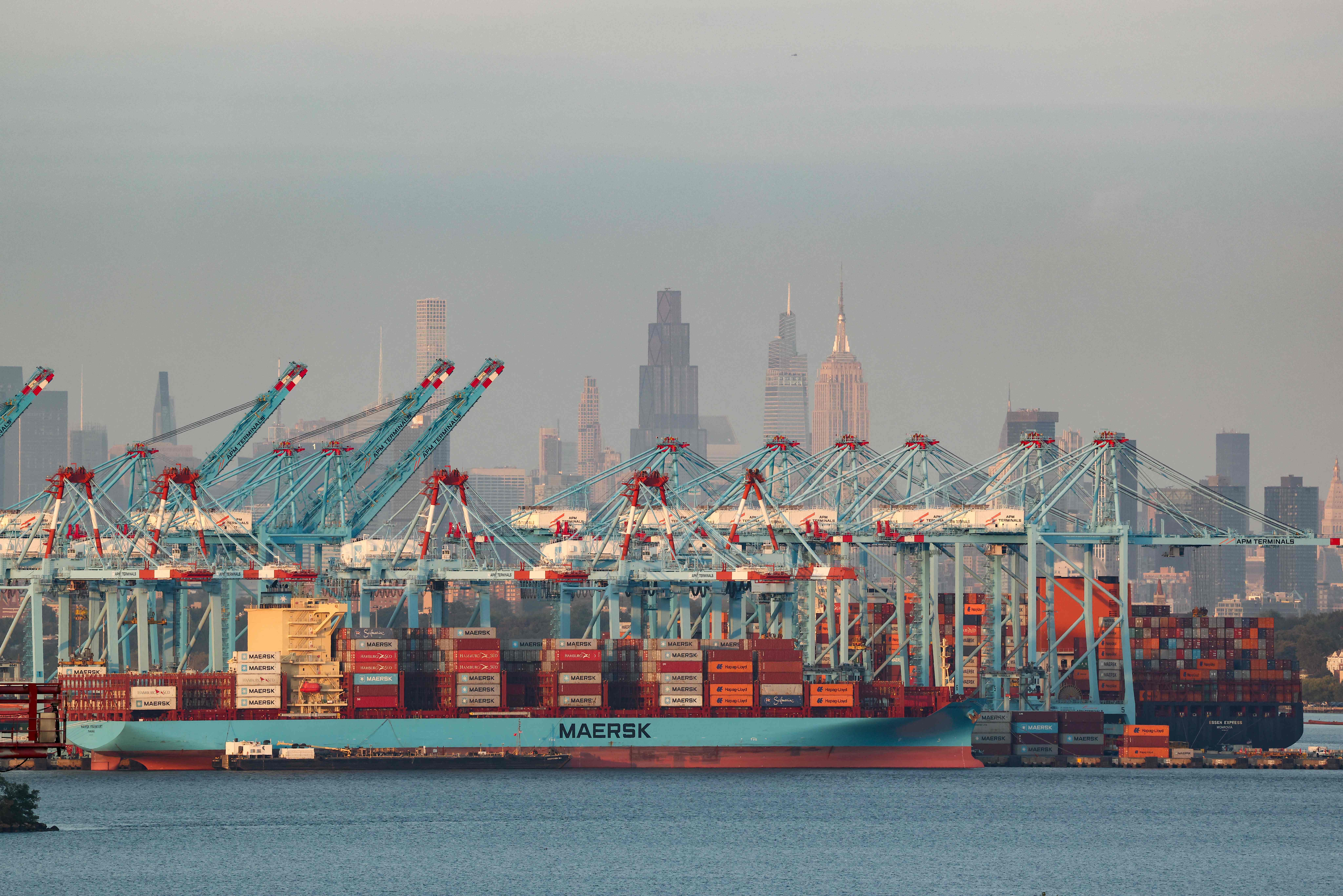 Cargo ships and shipping containers are seen at the Port Jersey Container Terminal, with the Manhattan skyline in the distance, in Jersey City, New Jersey on September 22, 2025. (Photo by CHARLY TRIBALLEAU / AFP)