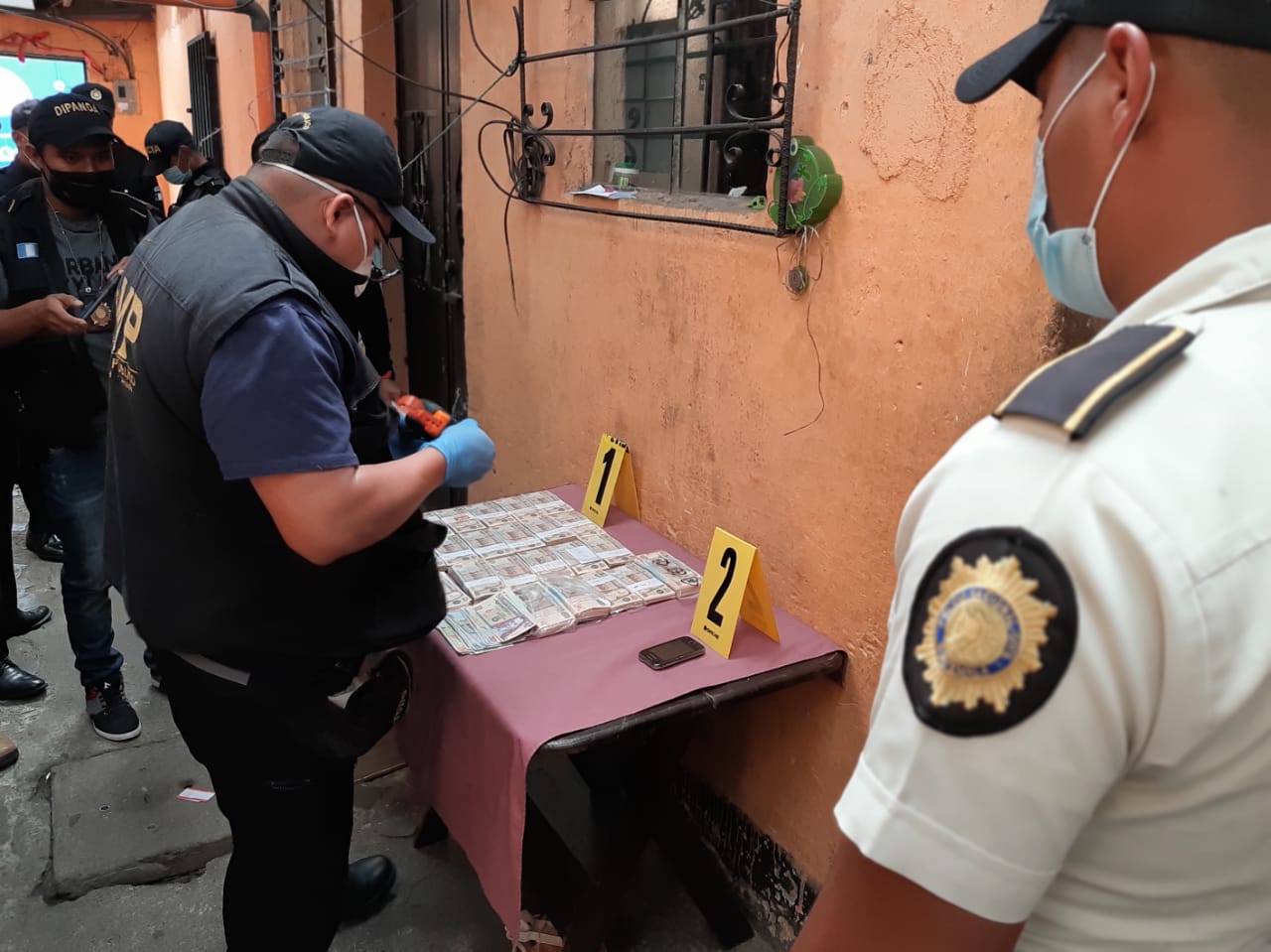 Oficiales durante un cateo incautan fajos de dinero en efectivo durante un allanamiento por denuncia de extorsión en Guatemala.