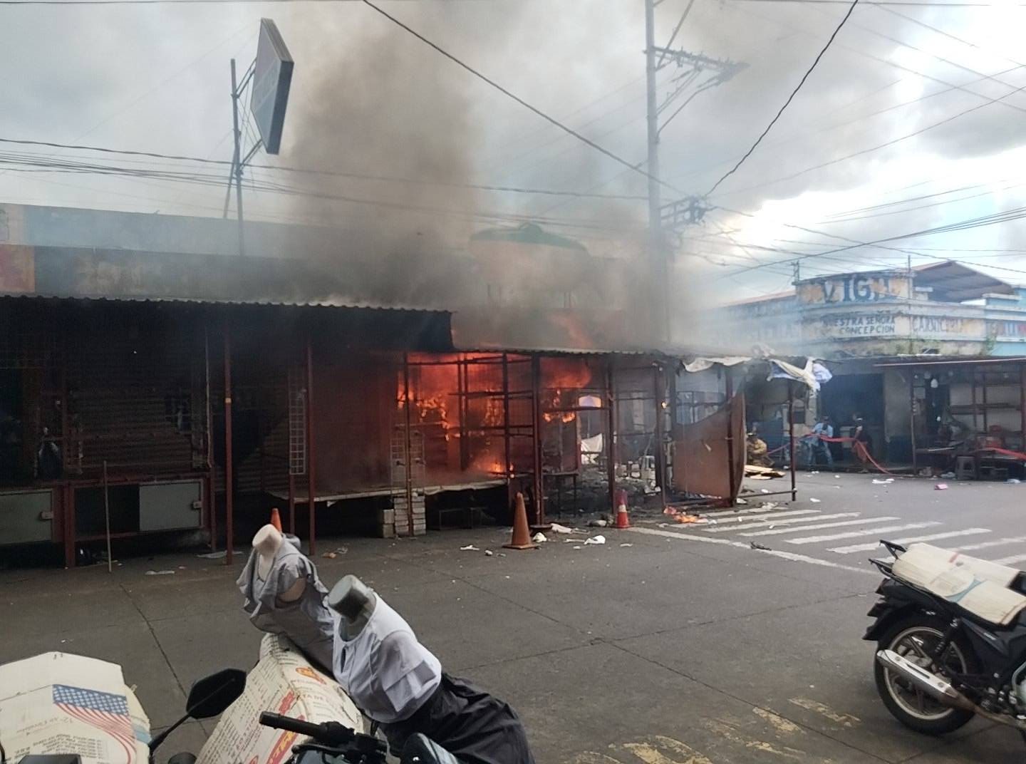 Humo denso invade las calles del centro de Escuintla mientras bomberos combaten un incendio en un depósito de pirotecnia. Comerciantes y vecinos observan desde la distancia.