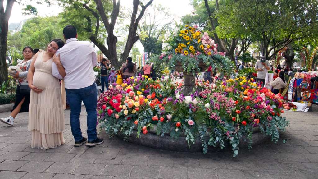 Pareja posa frente a una pequeña fuente del Parque Central de Antigua Guatemala; la mujer está embarazada.