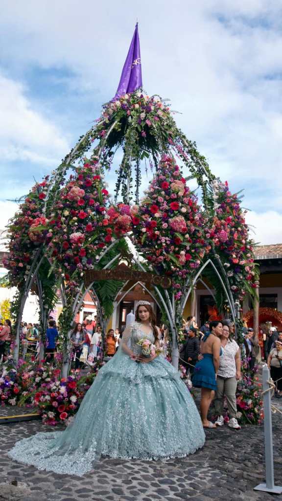 Quinceañera posa frente a una instalación floral en Antigua Guatemala.