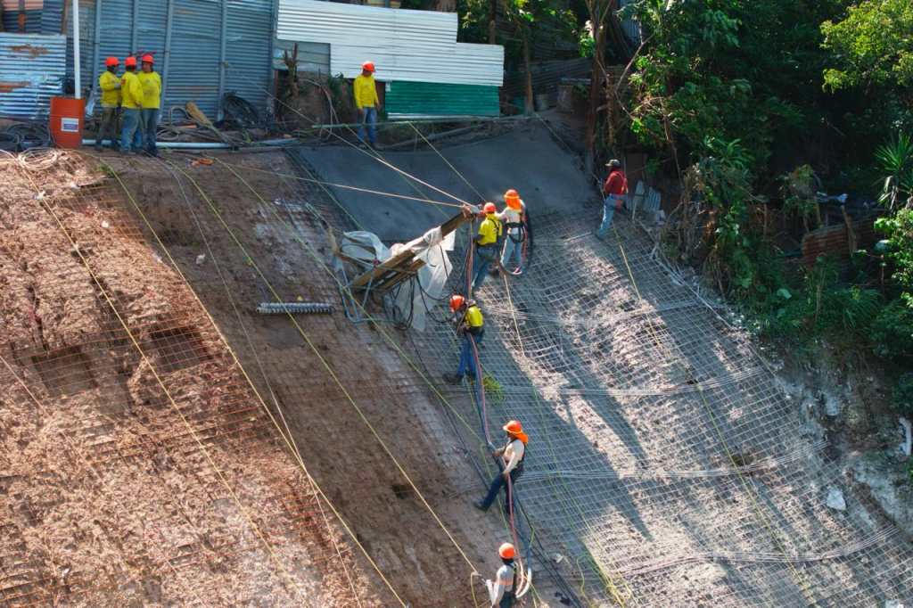 Trabajadores atados con cuerdas instalan electromalla en la ladera del km 11.5. 