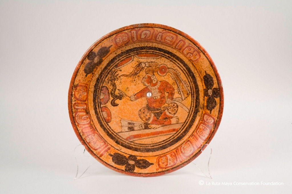 Plato decorado con un personaje sentado sobre una banca, con las piernas cruzadas. Viste tocado de plumas, joyería y pantalones de piel de jaguar. (Foto Prensa Libre: Fundación La Ruta Maya)