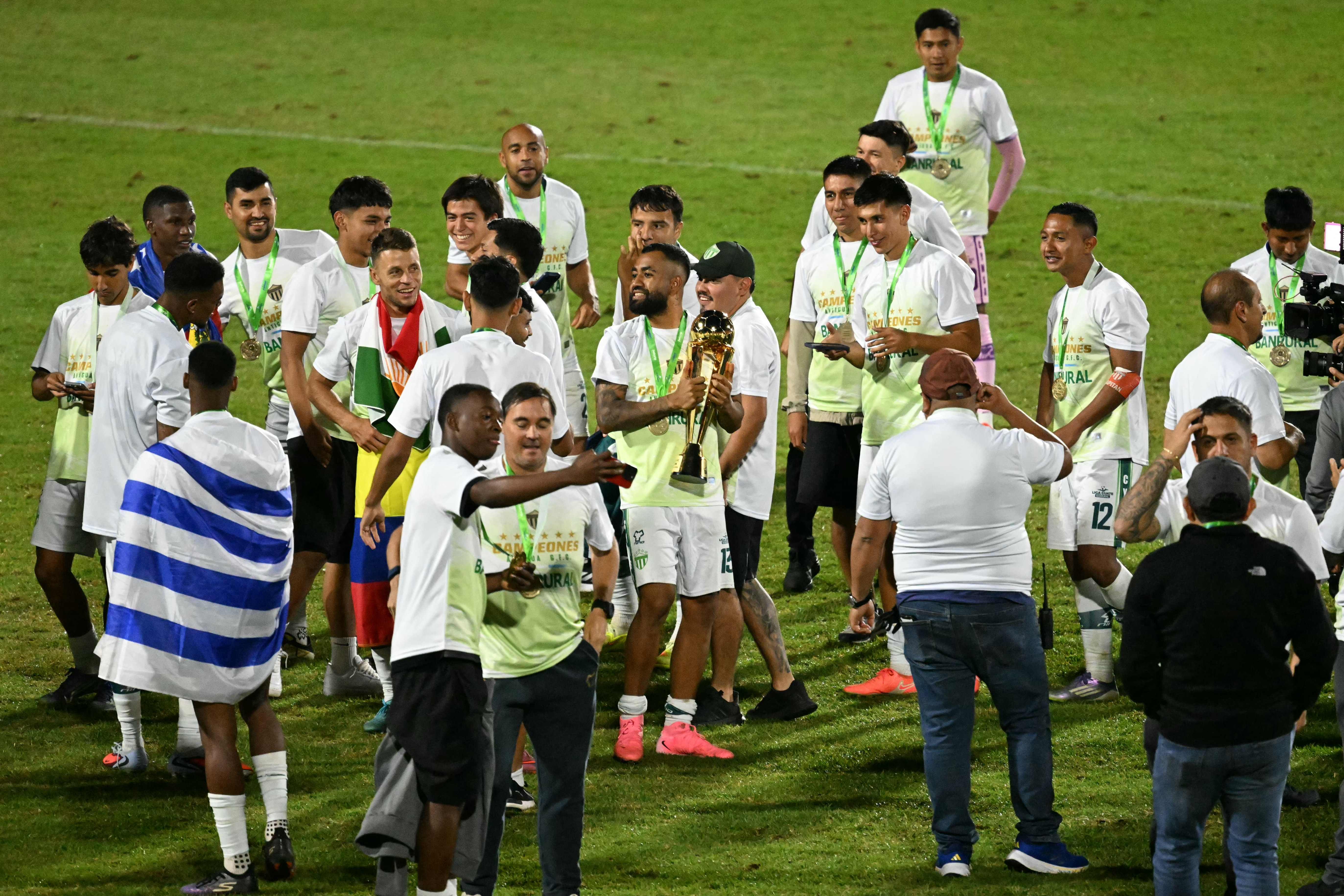 Antigua´s midfielder #13 Dewinder Bradley (C) holds the trophy next to teammates as they celebrate on the pitch after the Guatemalan Apertura tournament final second-leg football match between Municipal and Antigua at El Trebol Stadium in Guatemala City on December 27, 2025. (Photo by JOHAN ORDONEZ / AFP)
