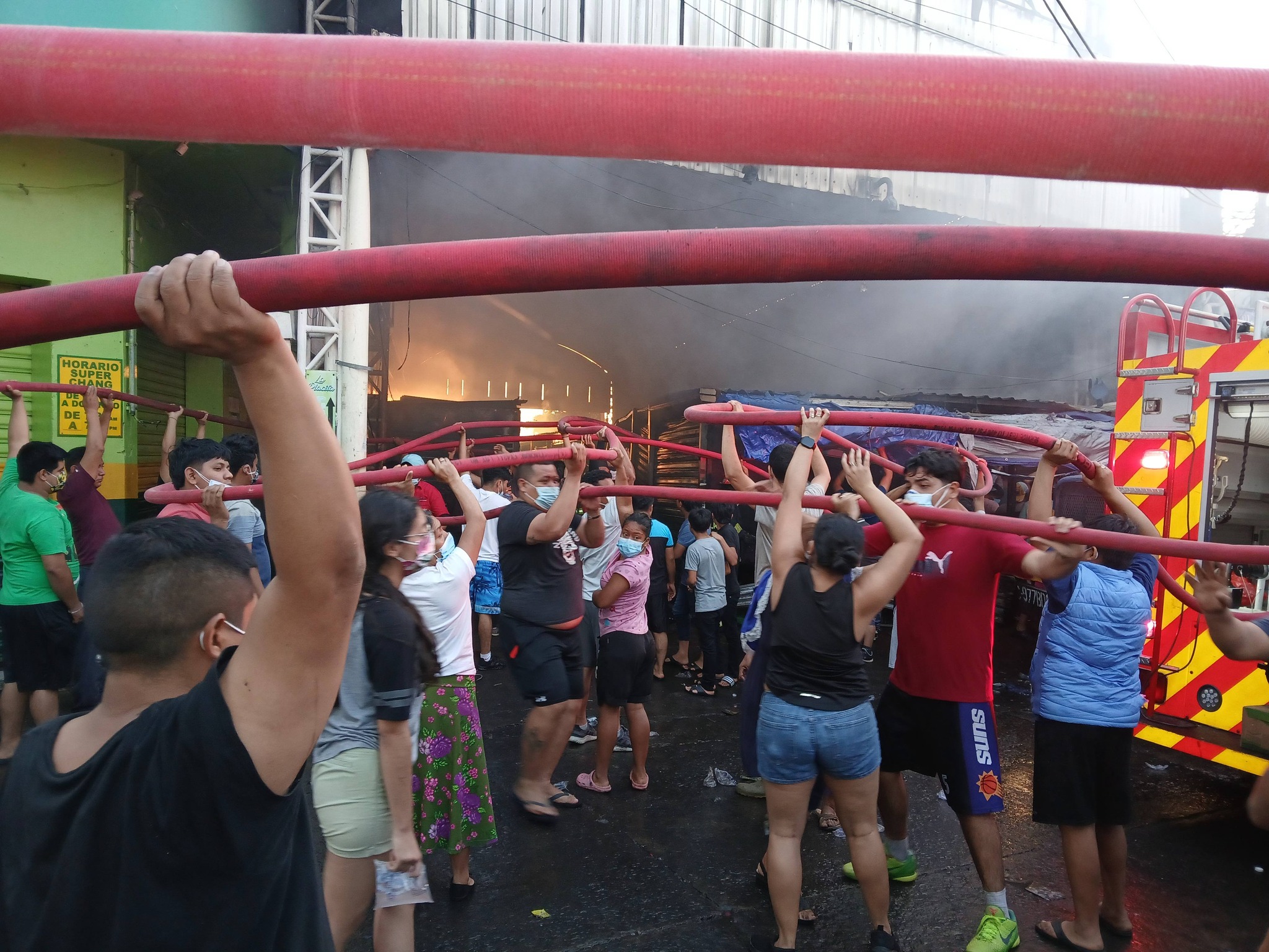 Personas apoyan a Bomberos Voluntarios sosteniendo mangueras para llevar agua al interior del mercado municipal de Chiquimulilla.