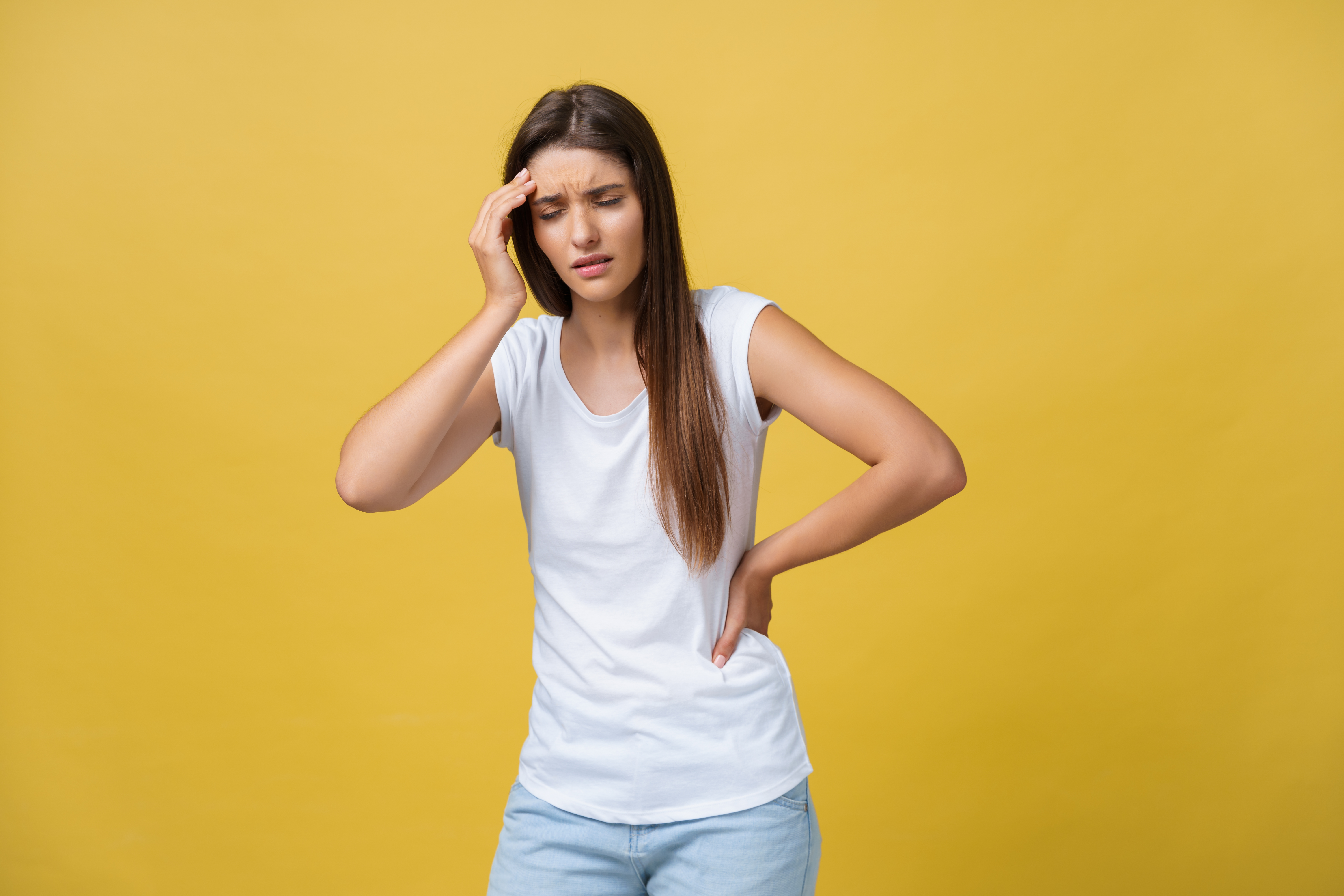 Young woman is suffering from a headache against a yellow background. Studio shot.