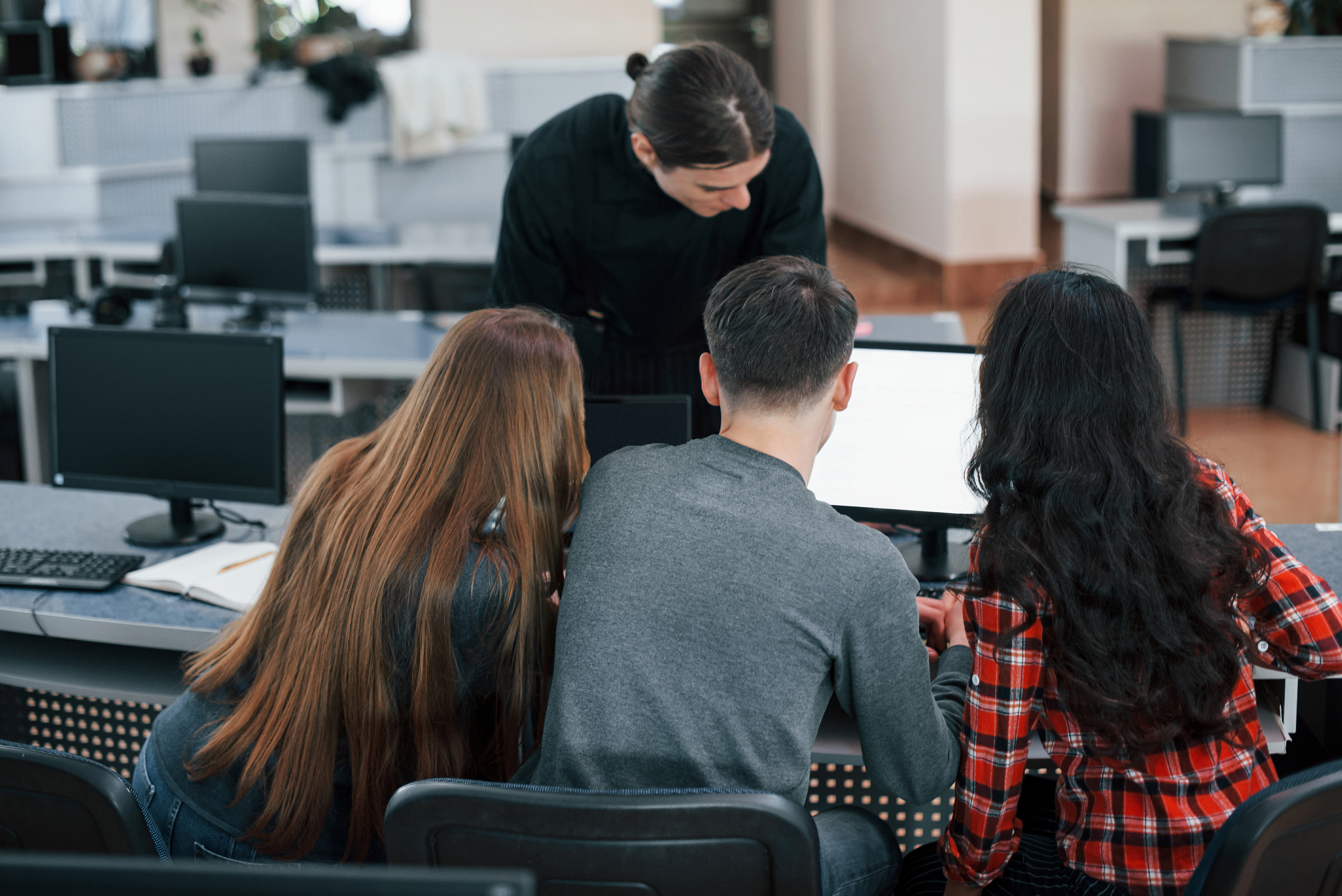 Together near one monitor. Group of young people in casual clothes working in the modern office.