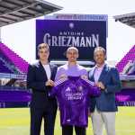 USA9339. ORLANDO (FL, EEUU), 24/03/2026.- Fotografía cedida por el Orlando City SC que muestra al futbolista francés Antoine Griezmann (c) sosteniendo la camisa del club junto a su propietario y presidente, Mark Wilf (d), y su director general y deportivo, Ricardo Moreira (i), este lunes en Orlando, Florida. El delantero Antoine Griezmann, máximo goleador de la historia del Atlético de Madrid, cerró este martes su fichaje por el Orlando City, con el que ha firmado por dos años más un tercero opcional y al que se incorporará a partir de la próxima temporada, en julio de 2026, una vez finalice el presente curso con el conjunto rojiblanco, según anunciaron ambos clubes en sendos comunicados. EFE/Mark Thor/Orlando City SC /- SOLO USO EDITORIAL/SOLO DISPONIBLE PARA ILUSTRAR LA NOTICIA QUE ACOMPAÑA (CRÉDITO OBLIGATORIO) -