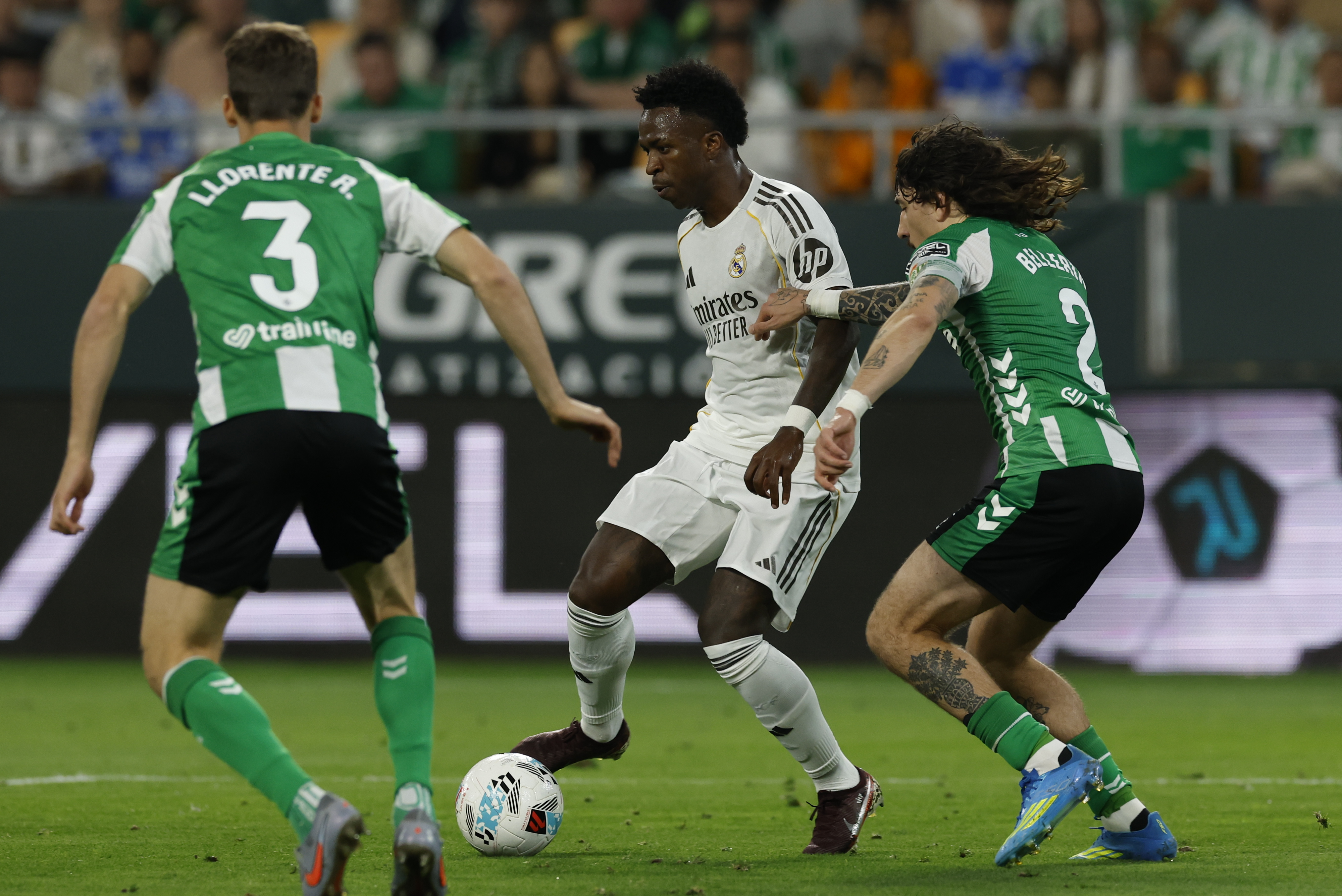 SEVILLA, 24/04/2026.- El delantero brasileño del Real Madrid, Vinicius Junior (c), con el balón ante el defensa del Betis, Héctor Bellerín, durante el encuentro correspondiente a la jornada 32 de Laliga EA Sports que disputan este viernes Betis y Real Madrid en el estadio de La Cartuja, en Sevilla. EFE / Julio Muñoz.