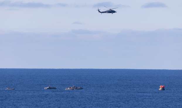 PACIFIC OCEAN (-), 10/04/2026.- A handout photo made available by the National Aeronautics and Space Administration (NASA) shows a US Navy MH-60 Seahawk from Helicopter Sea Combat Squadron (HSC) 23 flying overhead as small boats approach NASA's Orion spacecraft with Artemis II crewmembers after splashdown in the Pacific Ocean, 10 April 2026. The mission, crewed by NASA astronauts Reid Wiseman, commander, Victor Glover, pilot, Christina Koch, mission specialist, and CSA (Canadian Space Agency) astronaut Jeremy Hansen, mission specialist, completed a flyby of the Moon and returned to Earth. EFE/EPA/JOEL KOWSKY / NASA / HANDOUT HANDOUT EDITORIAL USE ONLY/NO SALES