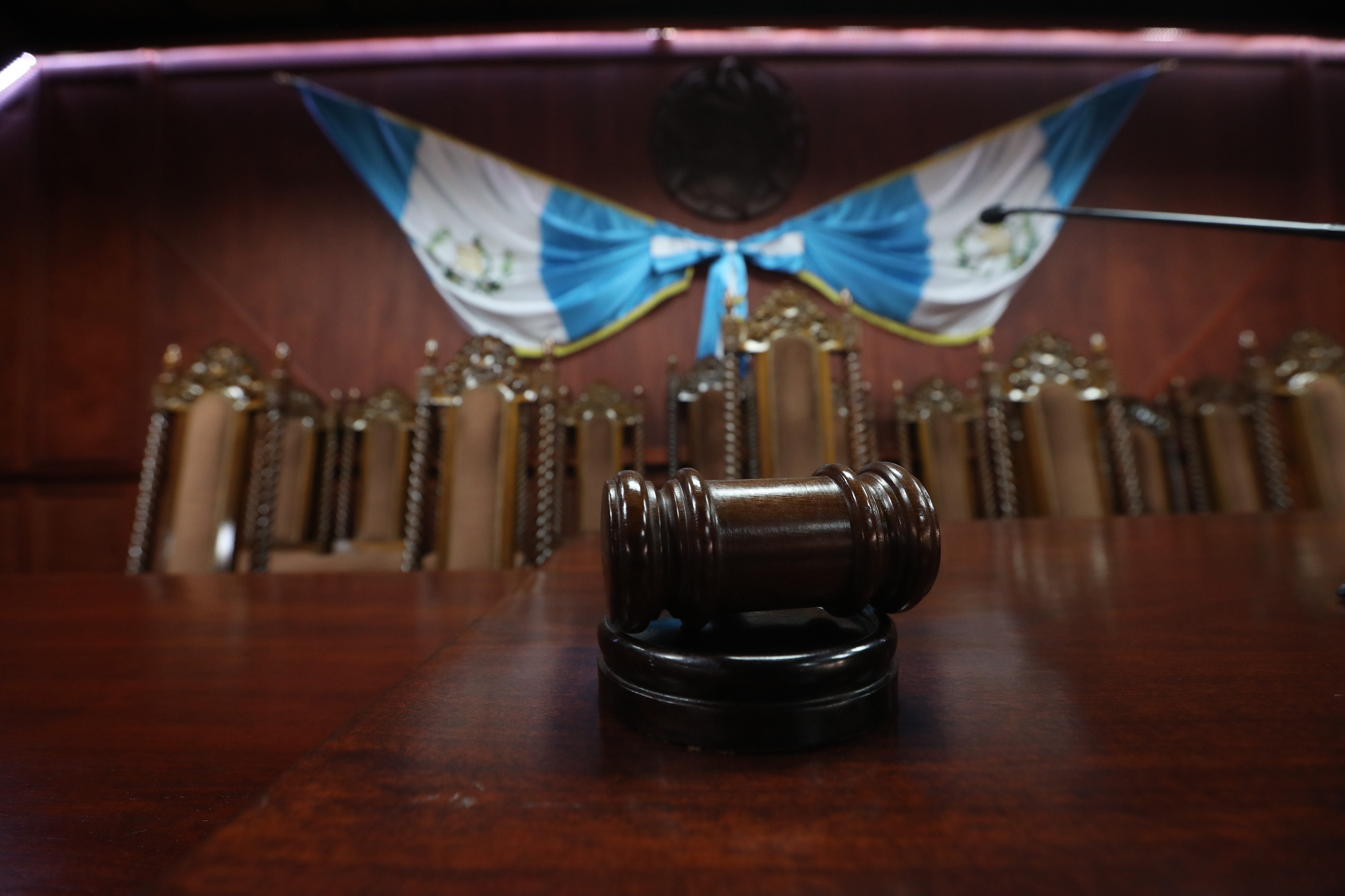 Pleno de magistrados en sala de sesiones con sillas vacías y mazo de autoridad sobre la mesa