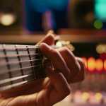 Artist composer creating a new song on his electro guitar in studio, recording tracks in control room using mixing console and amplifier. Songwriter creates new music for his album. Camera B.