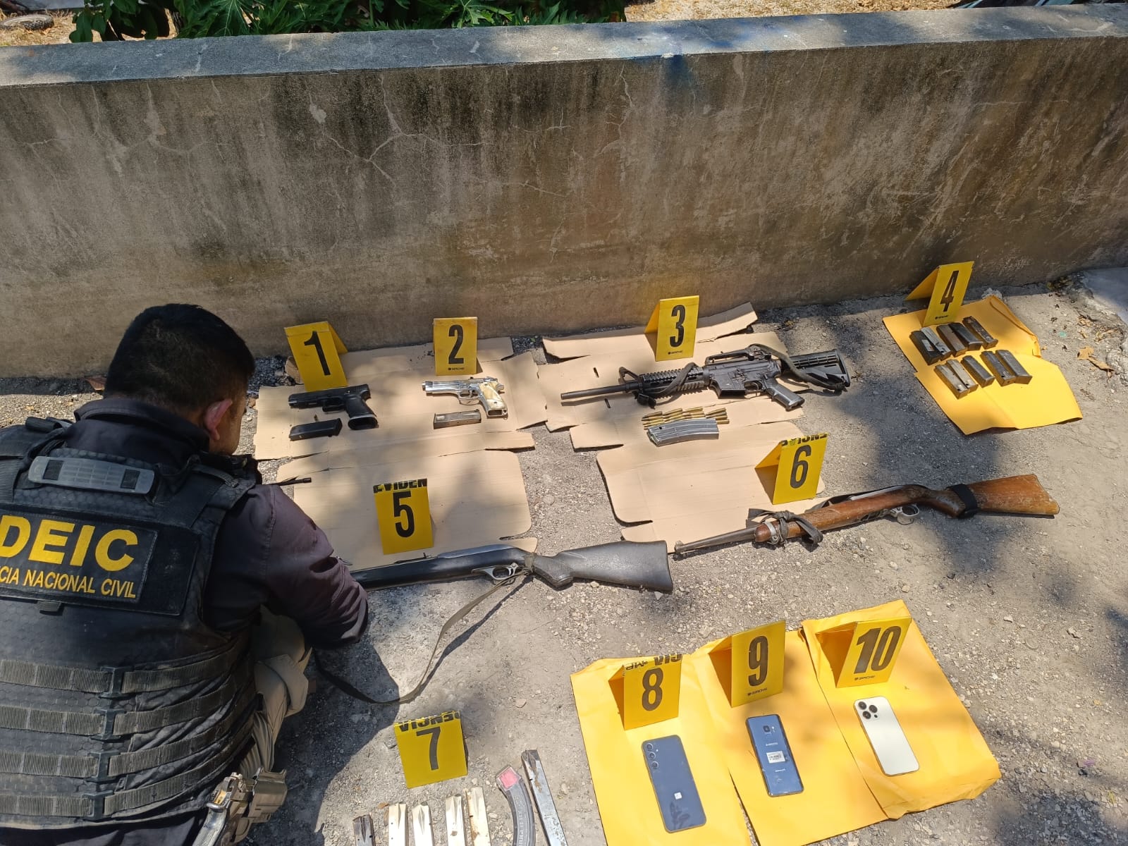 Agente policial marca armas como evidencia durante cateo en operativo de investigación