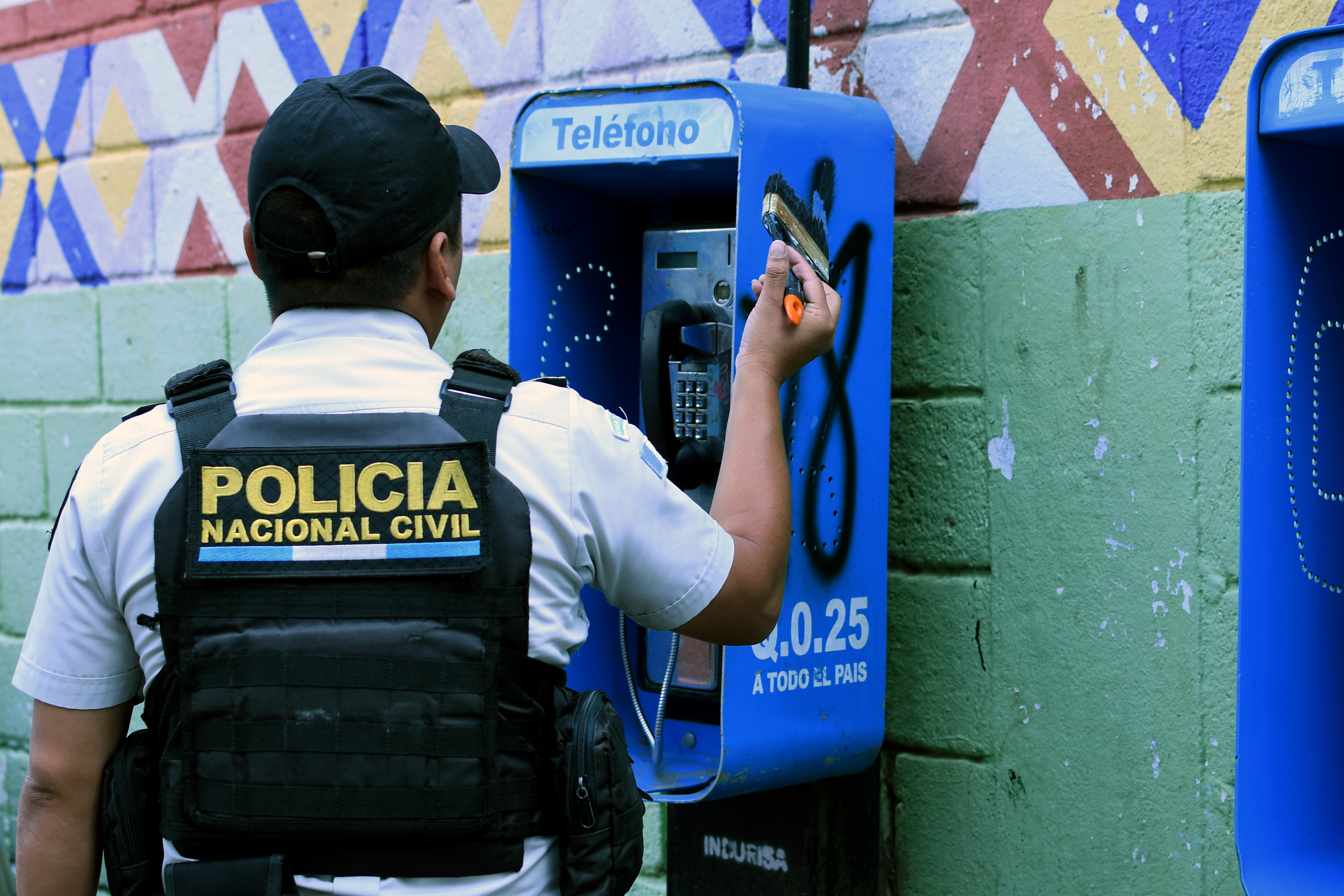 Agente de la PNC borra mensajes de la pandilla Barrio 18 en muros y teléfonos públicos en Mixco.