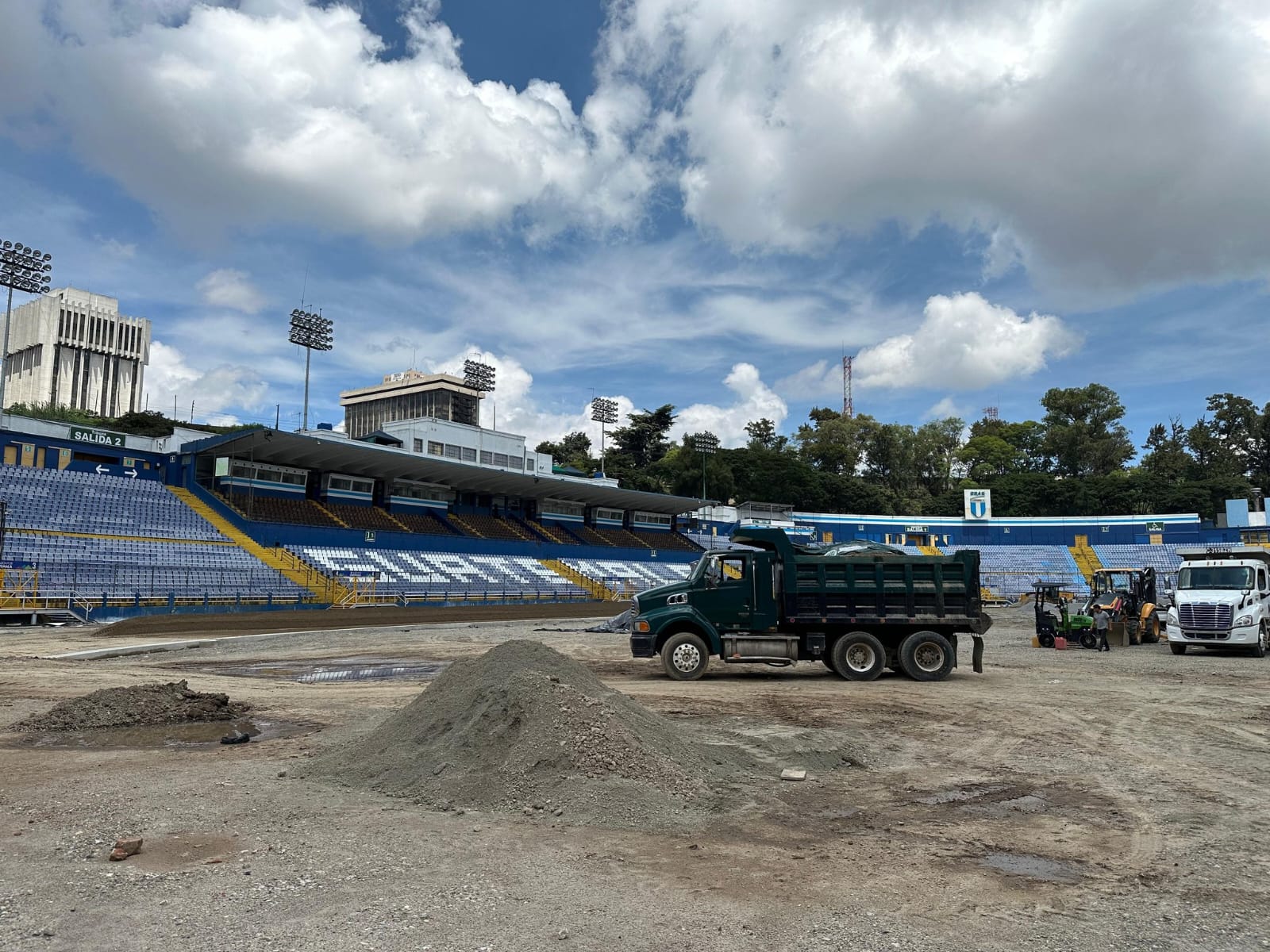Camión trabaja en el centro del campo del estadio durante las obras de remodelación, con suelo de tierra y piedrín. Fotografía de mayo 2026.