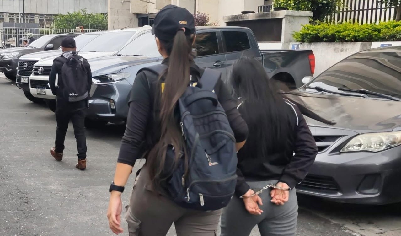 Una de las siete mujeres capturadas durante los allanamientos por un caso de extorsión es trasladada por agentes de la PNC. (Foto Prensa Libre: PNC) 