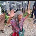 Tras el desalojo de su vivienda, Juana Santiago Chel permanece sentada frente a agentes de la PNC en Nebaj, Quiché. (Foto Prensa Libre: Captura de video)