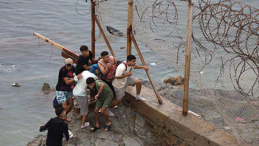 Hombres sobre un montón de rocas junto al mar en la frontera entre Marruecos y España.
