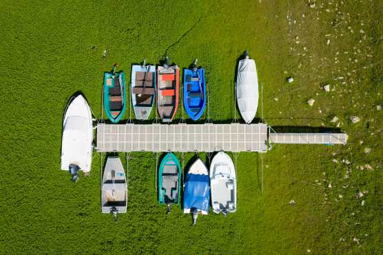 Les Brenets (Switzerland), 22/08/2026.- An aerial view shows stranded boats trapped in a mud-covered area with green grass on the dried out shore of the Lac des Brenets, its Swiss name, or Lac de Chaillexon, the French name, in Les Brenets, Switzerland, 22 August 2026. The lake sits on the Doubs river, a natural border between eastern France and western Switzerland. (sequía, Francia, Suiza) EFE/EPA/PETER KLAUNZER