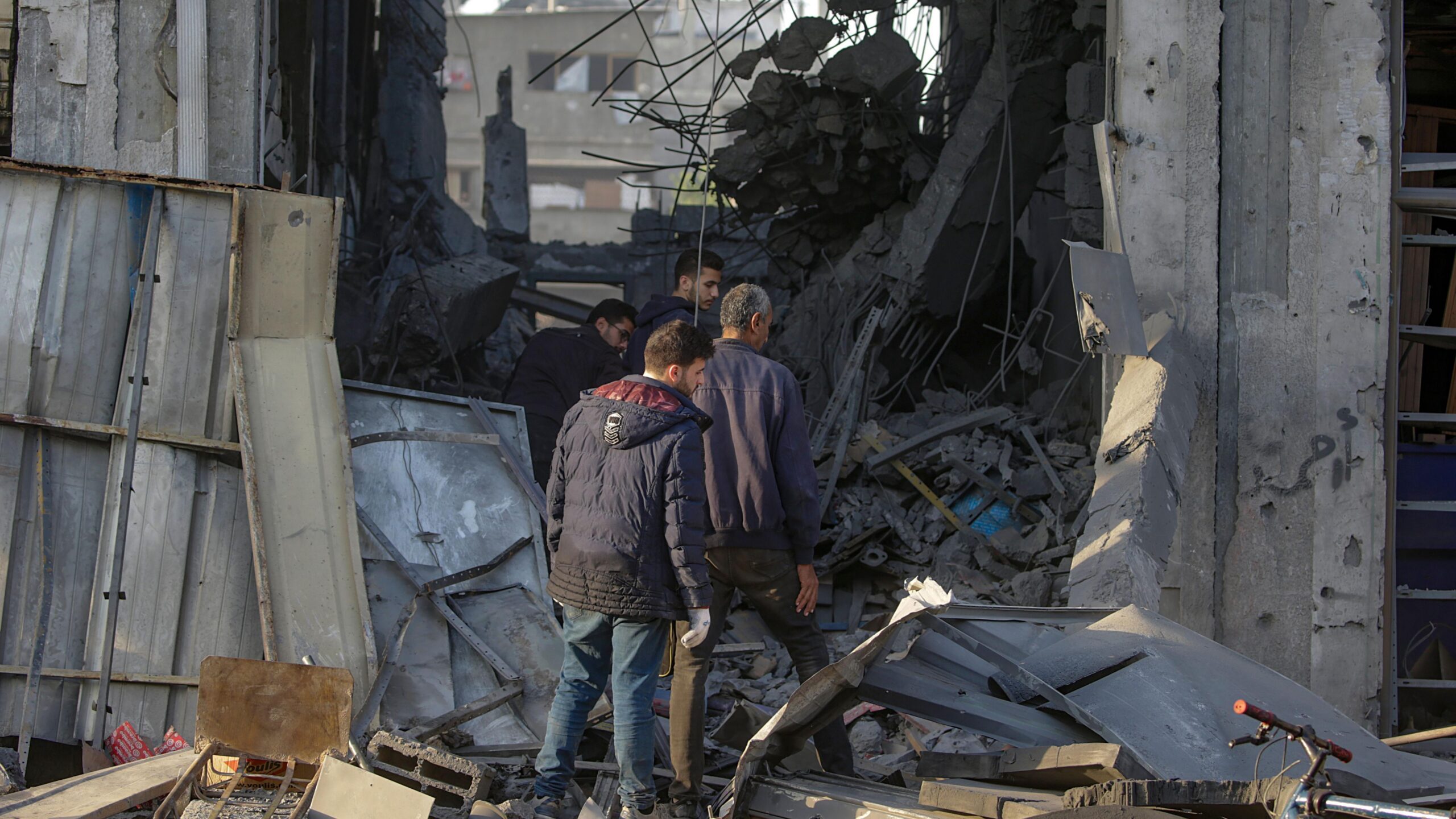 Un niño pequeño observa un bloque amarillo colocado entre escombros en Gaza. Al fondo, se ve una barrera de tierra junto a un edificio en escala azul dentro de un marco azul de BBC Verify.
