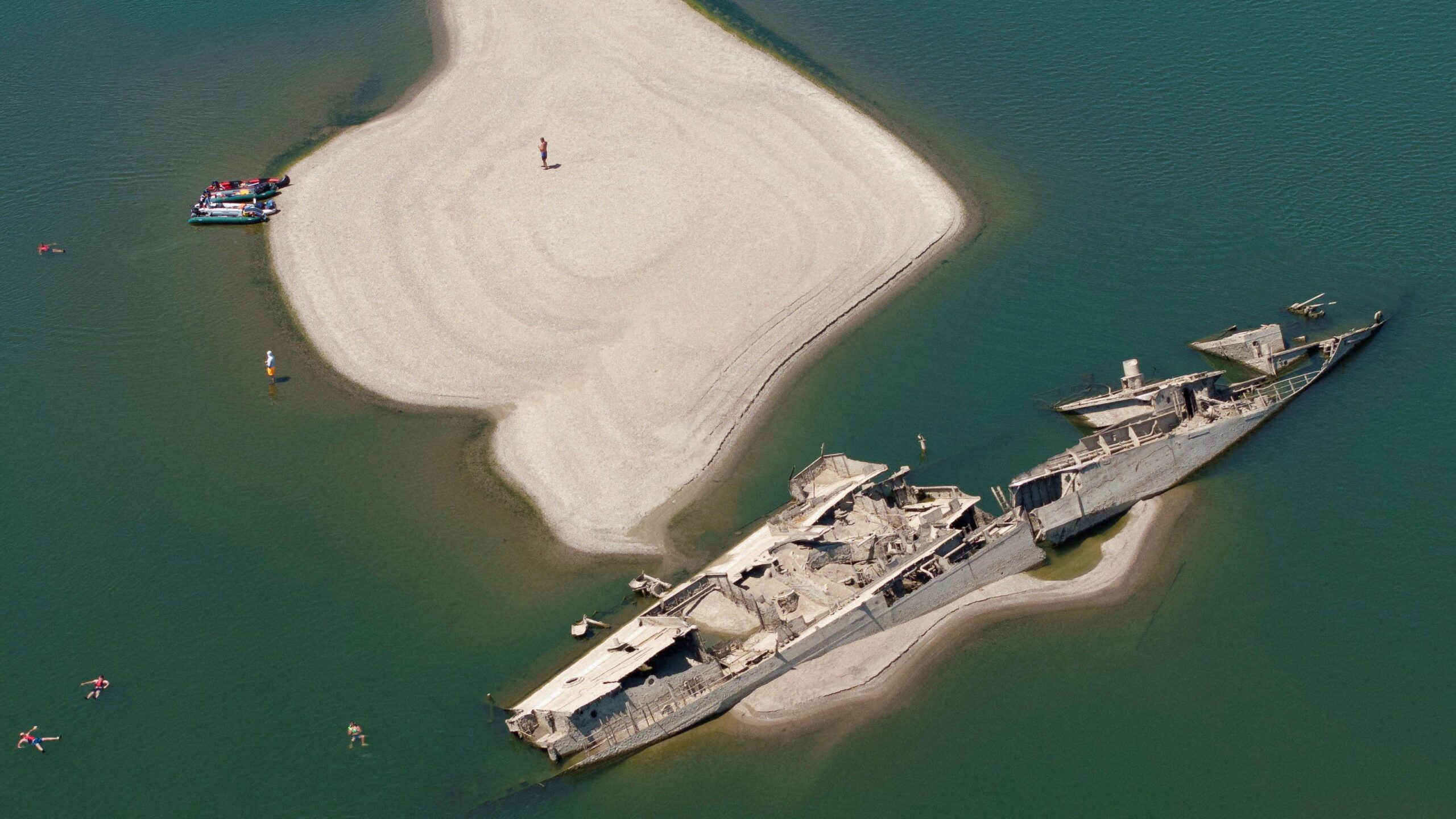 A large shipwreck is visible next to a white sandbank in green waters.