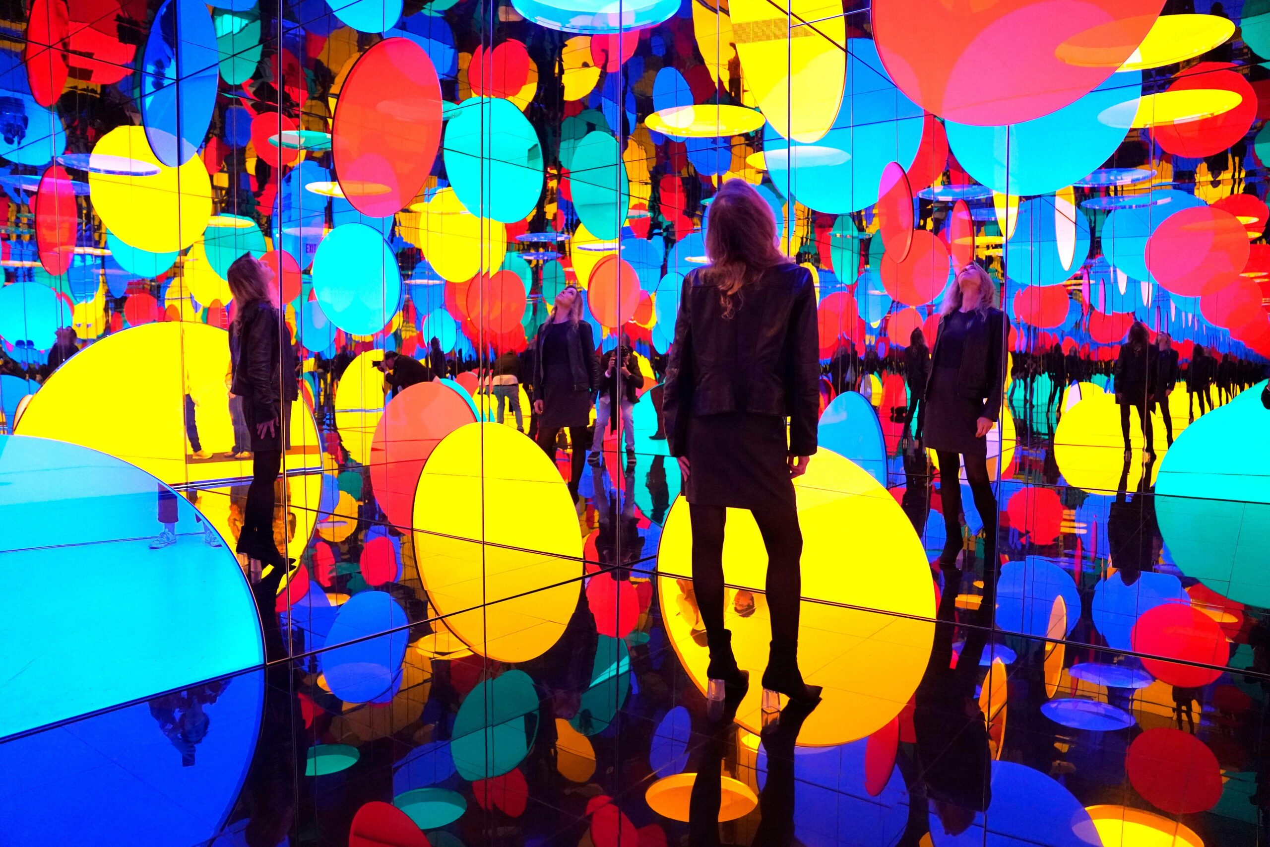 Yayoi Kusama seen looking through a clear screen with red spots painted on it, with red and white clothes and background