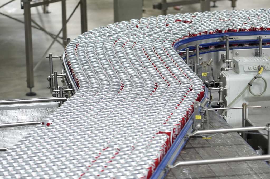 Línea de producción automatizada trasladando latas de bebidas en la planta de Coca-Cola ABASA en Río Hondo, Zacapa.