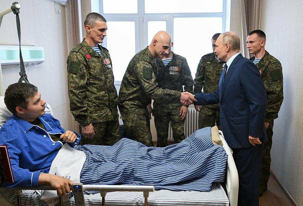 Una imagen del presidente de Rusia, Vladimir Putin, saludando con la mano. En primer plano, diez soldaditos de juguete de color verde oscuro rodean una bandera rusa en miniatura.