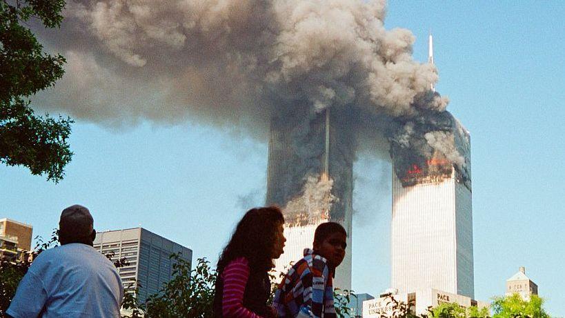 Las Torres Gemelas en segundo plano, ardiendo, en primer plano tres personas mirando.