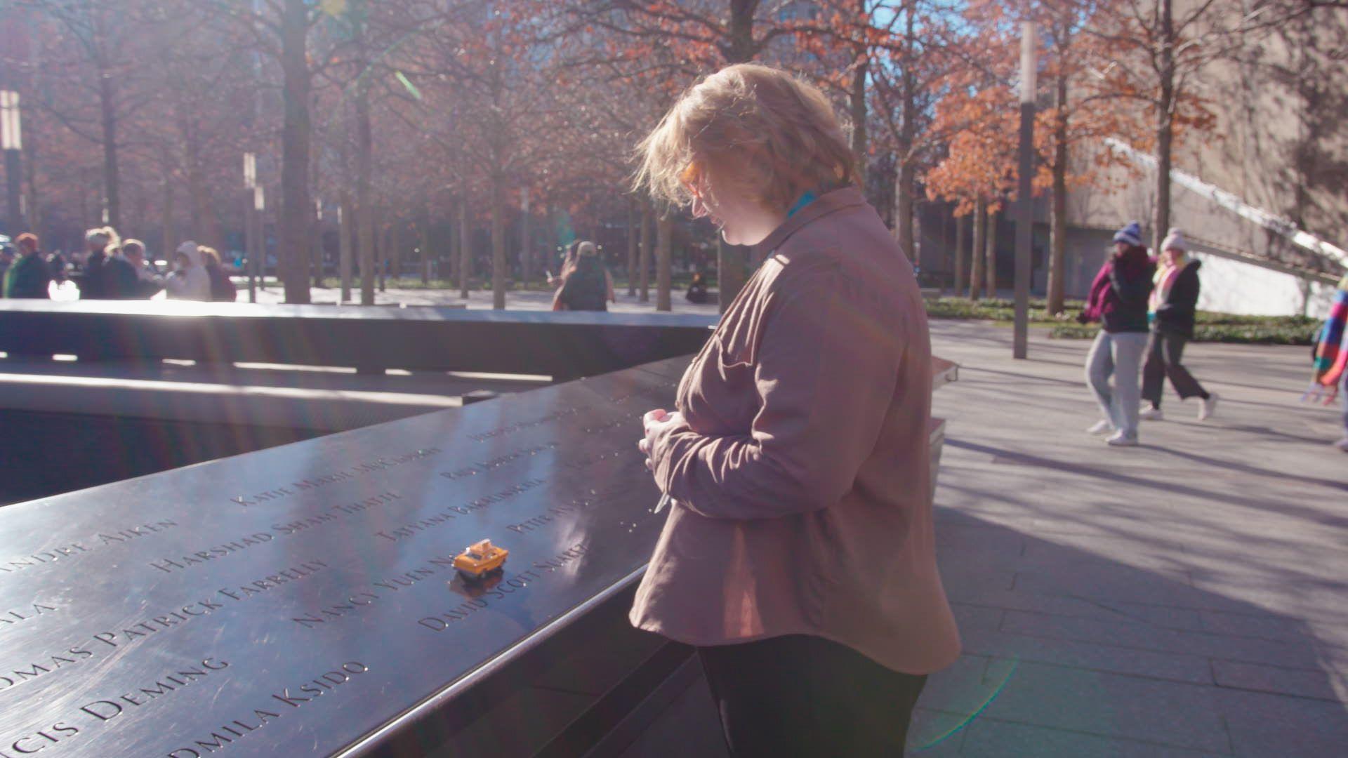 Alicia Esteve Head que se hizo pasar por una víctima del 11-S posa con el cabello rubio y gafas de pasta negra frente a una maqueta de las Torres Gemelas.