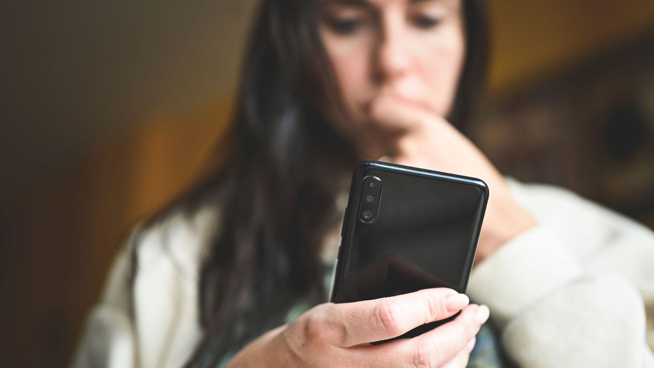 Una imagen de archivo de una mujer que mira su teléfono inteligente, mordiéndose las uñas nerviosamente.