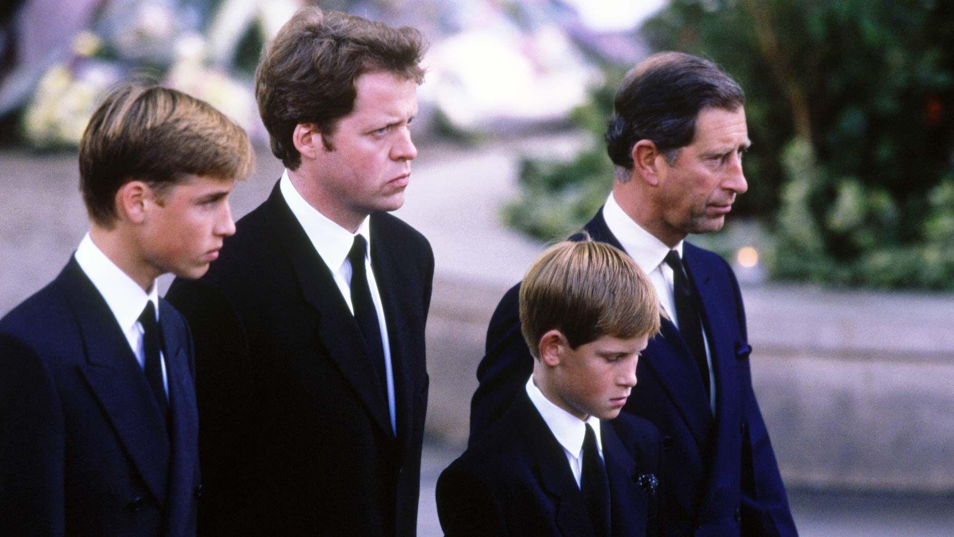 El joven príncipe William aparece junto a Earl Spencer, el joven príncipe Harry y Carlos en el funeral de Diana. Todos visten trajes oscuros con corbata y miran al frente con solemnidad.