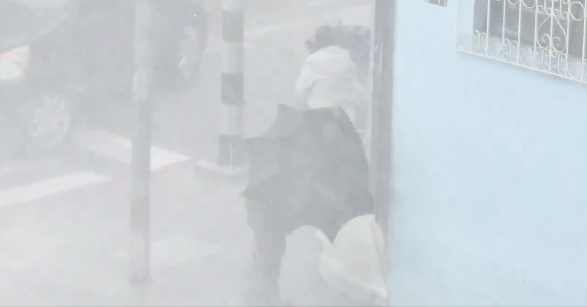 Dos personas buscan resguardarse de la fuerte lluvia que afecta un sector de la zona 1 de la capital durante la tormenta de este lunes. (Foto Prensa Libre: Captura de pantalla)