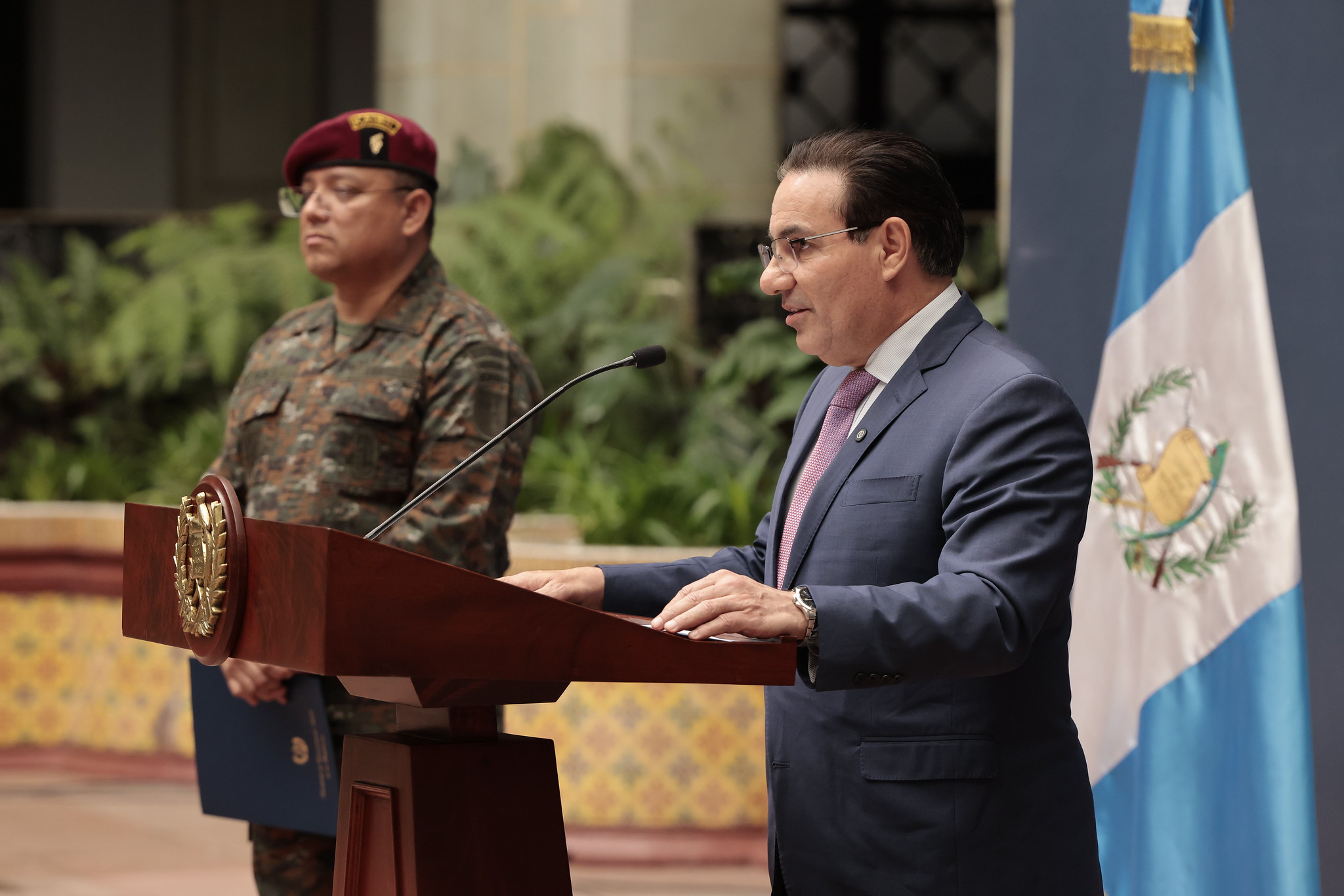 Ministro de Gobernación Marco Villeda en podio junto al ministro de la Defensa Henry Saenz durante conferencia sobre bloqueos en Guatemala.