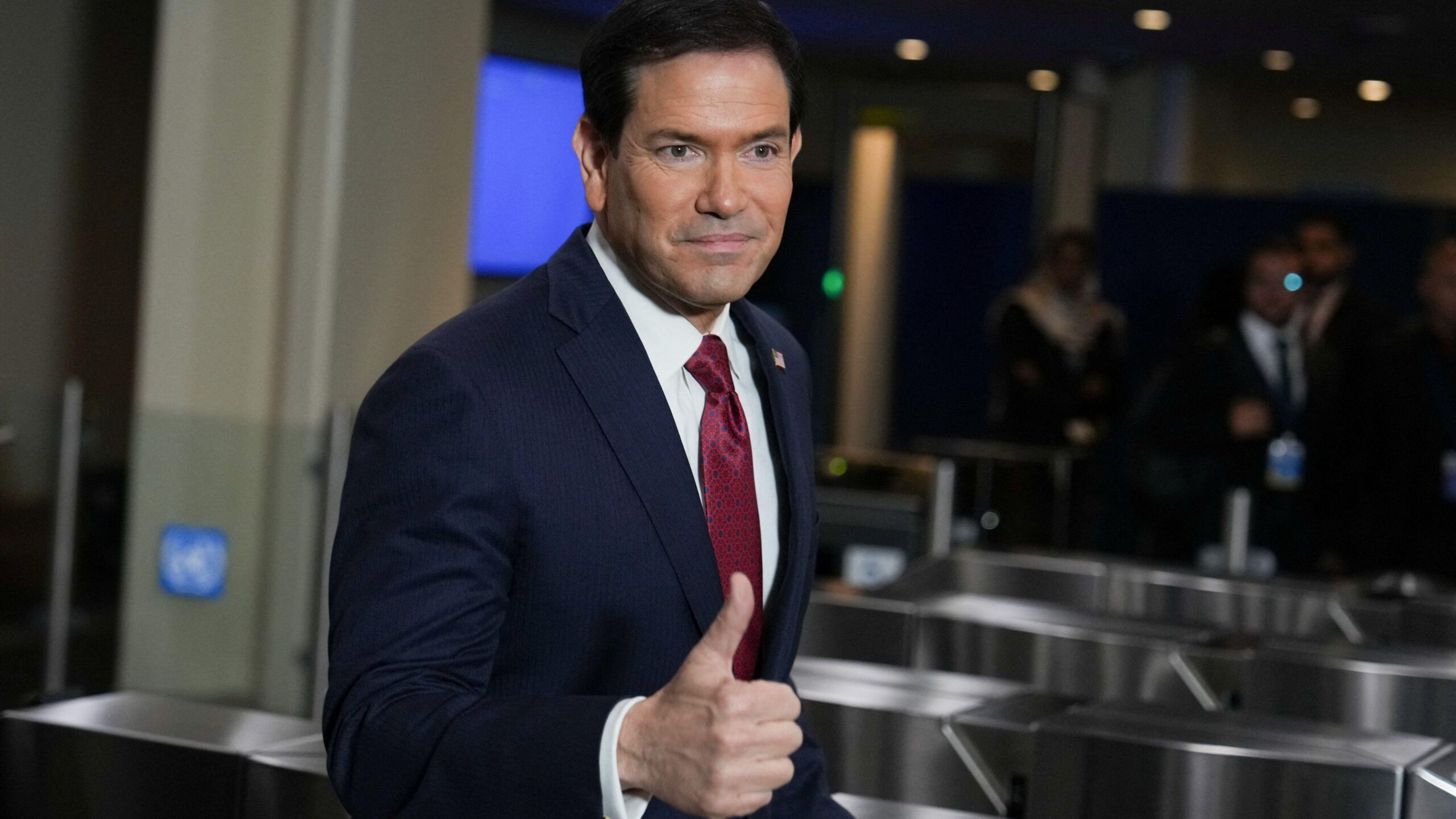 Juan Omar Sixto posa frente a una piscina y la bahía de Biscayne en Miami. Viste elegantemente con traje y corbata.