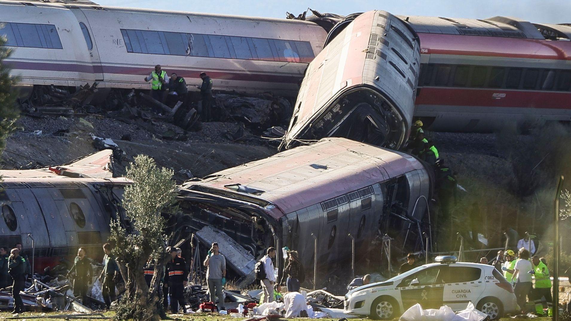 Dos trenes destrozados tras el choque en España. Uno de los convoyes muestra tres vagones volcados sobre el rerraplén contiguo a la vía. Junto a los restos de los trenes, trabajan decenas de efectivos de emergencia. En el suelo hay bolsas blancas, aparentemente de las que se usan para transportar restos humanos. Junto a ellas hay un auto policial.