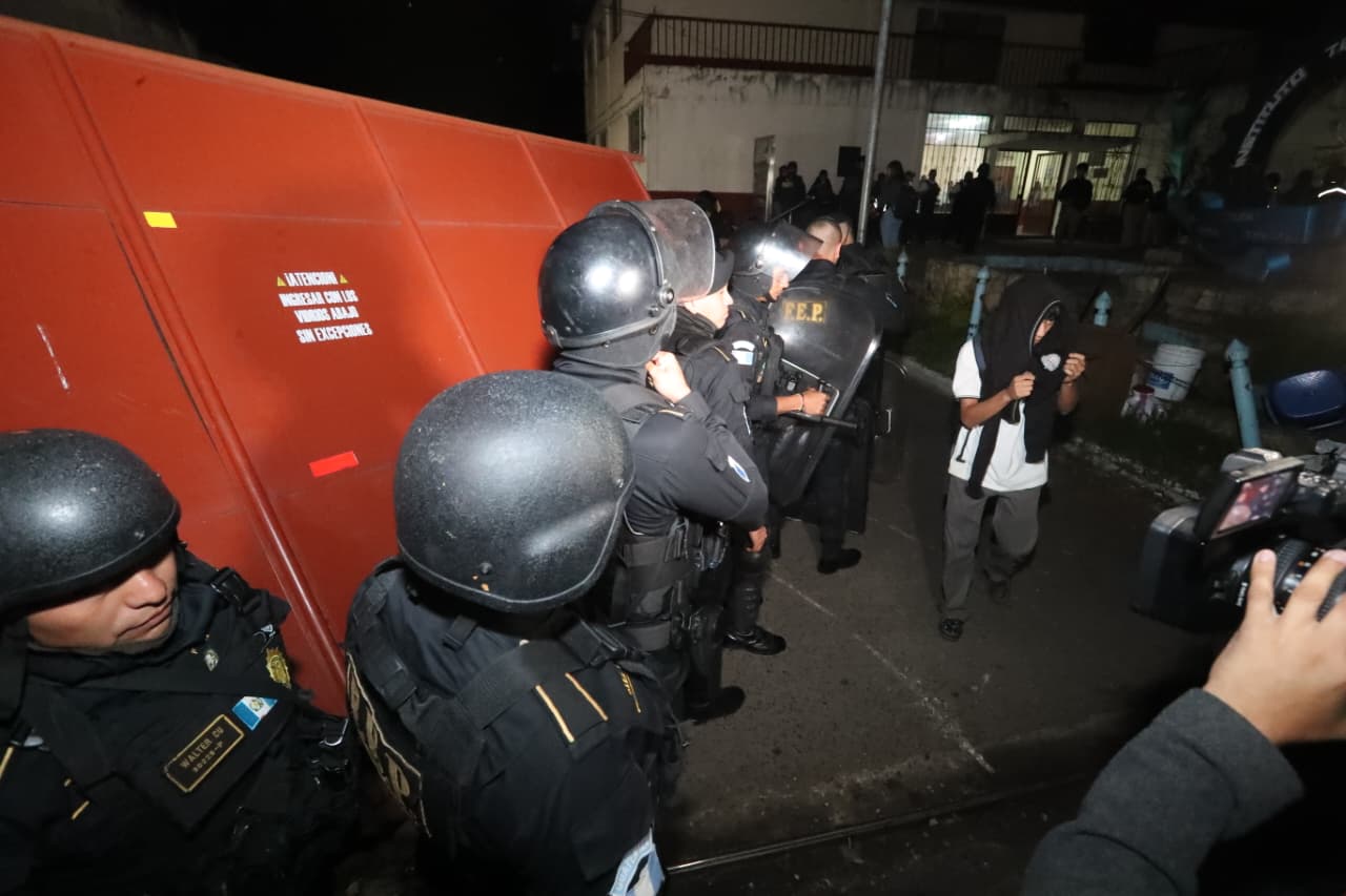 Agentes de la PNC, equipados con cascos y escudos, permanecen frente a un portón del Instituto Fischmann durante el allanamiento del MP. (Foto Prensa Libre: Juan Diego González)