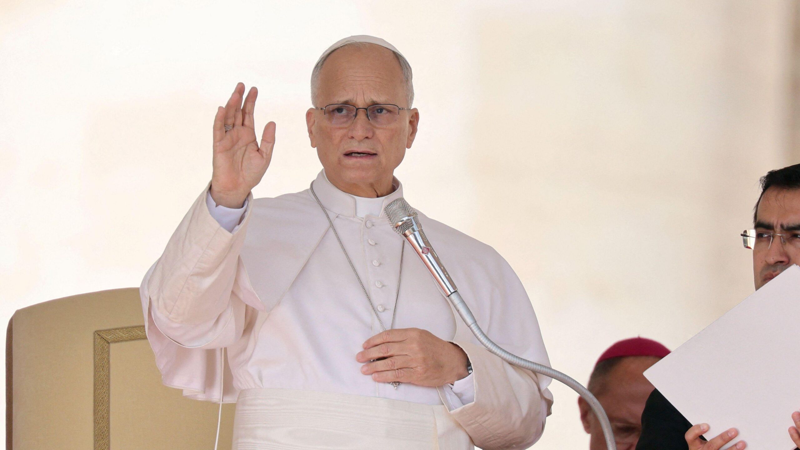 El papa León habla por un micrófono y levanta la mano.
