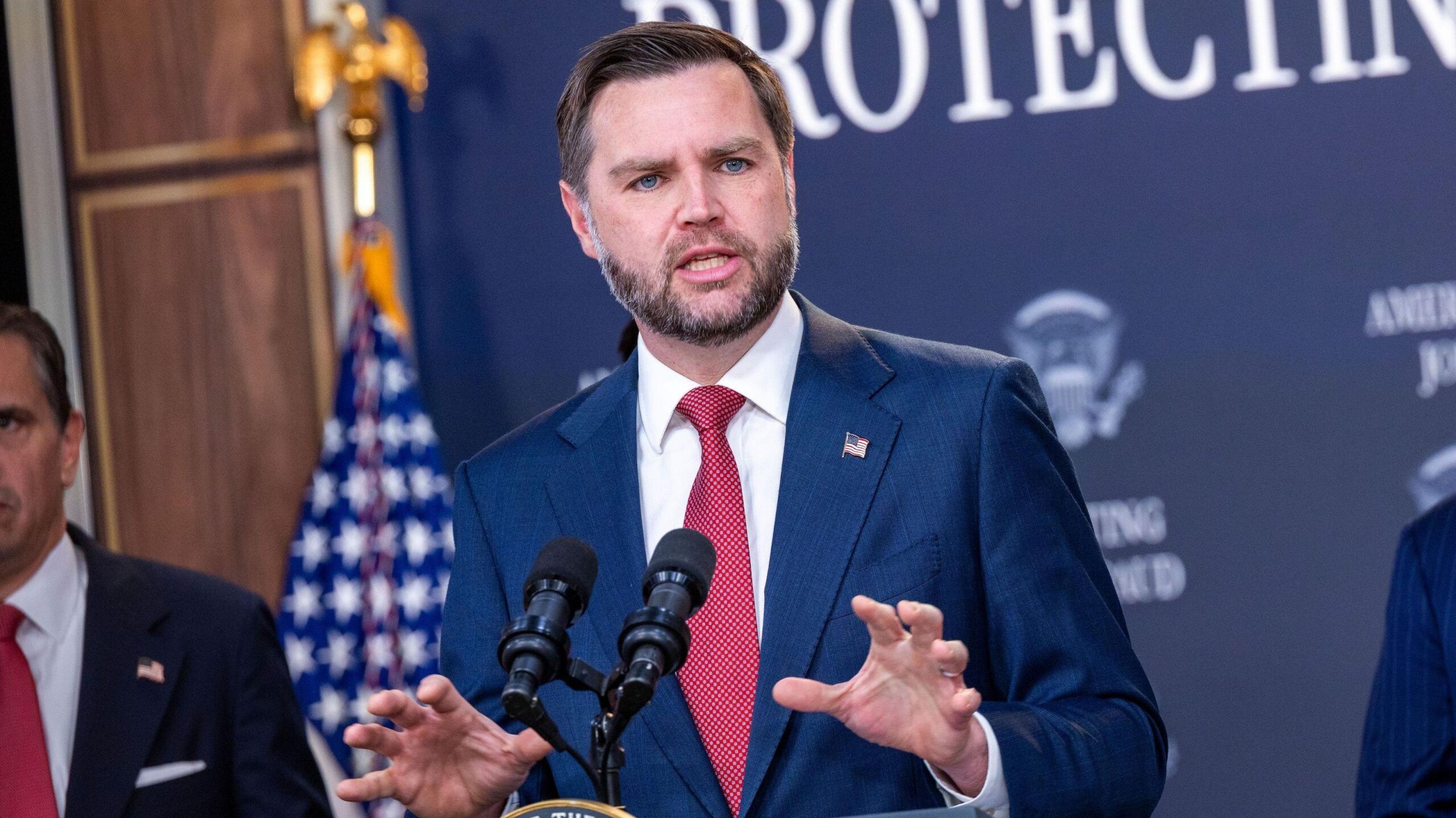 El vicepresidente JD Vance, de pie en un podio y gesticulando, vestido con un traje azul, camisa blanca y corbata roja.