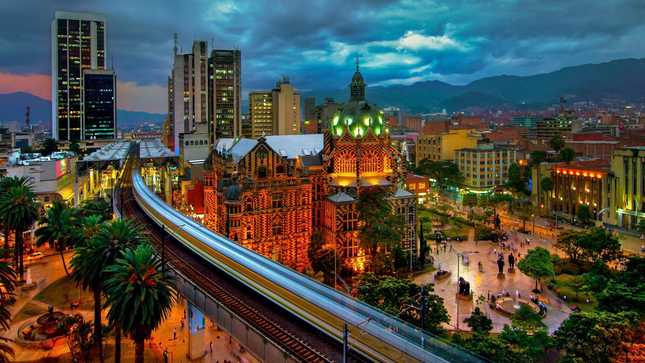 Vista aérea del metro de Medellín pasando por la Plaza Botero, en el centro de la ciudad, al atardecer.