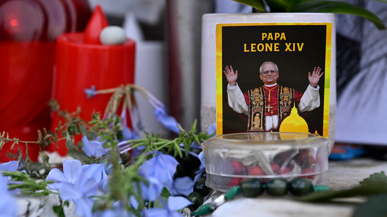 Unas flores azules, velas rojas y una foto del Papa León XIV están bajo una estatua del Papa Juan Pablo II afuera del Policlínico Gemelli, donde el Papa León XIV se está recuperando de la cirugía a la que se sometió el martes.