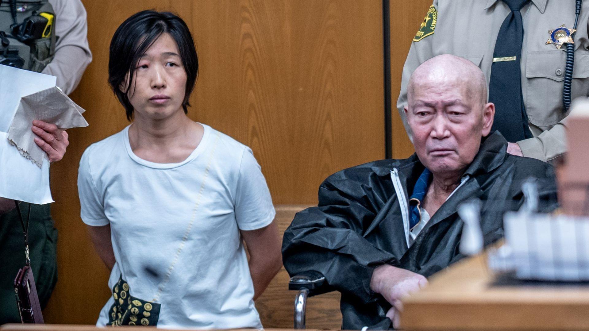 Silvia Zhang, a la izquierda, y Guojun Xuan, a la derecha, sentados en la sala del tribunal de Pasadena con dos alguaciles de pie detrás de ellas. Zhang tiene la mano detrás de la espalda y lleva una camisa azul, mientras que Xuan lleva una chaqueta negra.