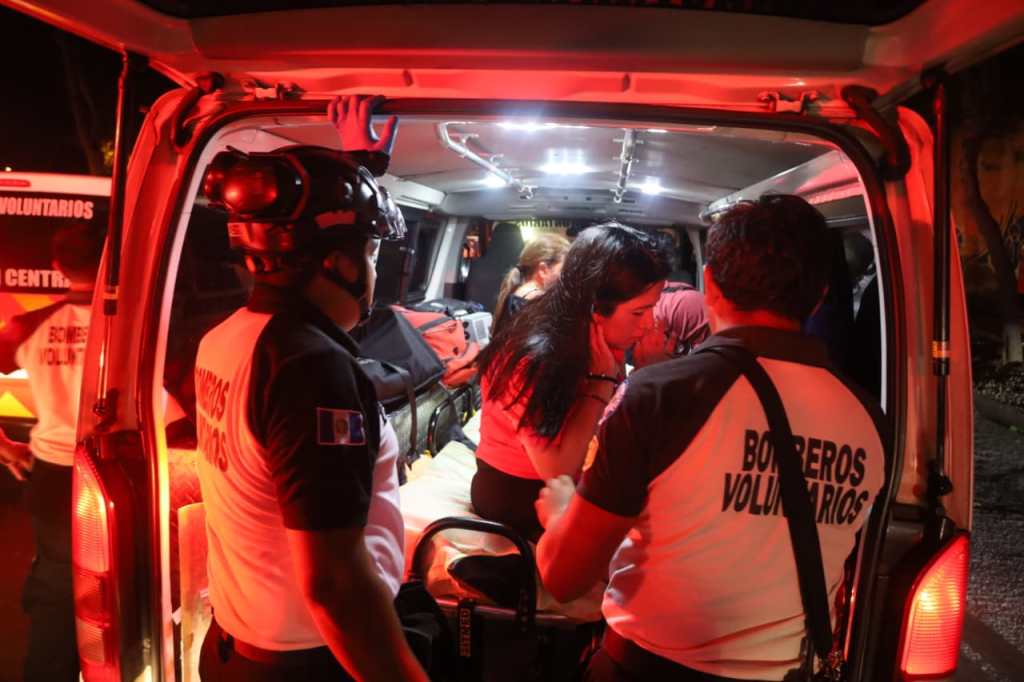 Bomberos Voluntarios atienden a personas heridas dentro de una ambulancia tras la caída de un árbol.